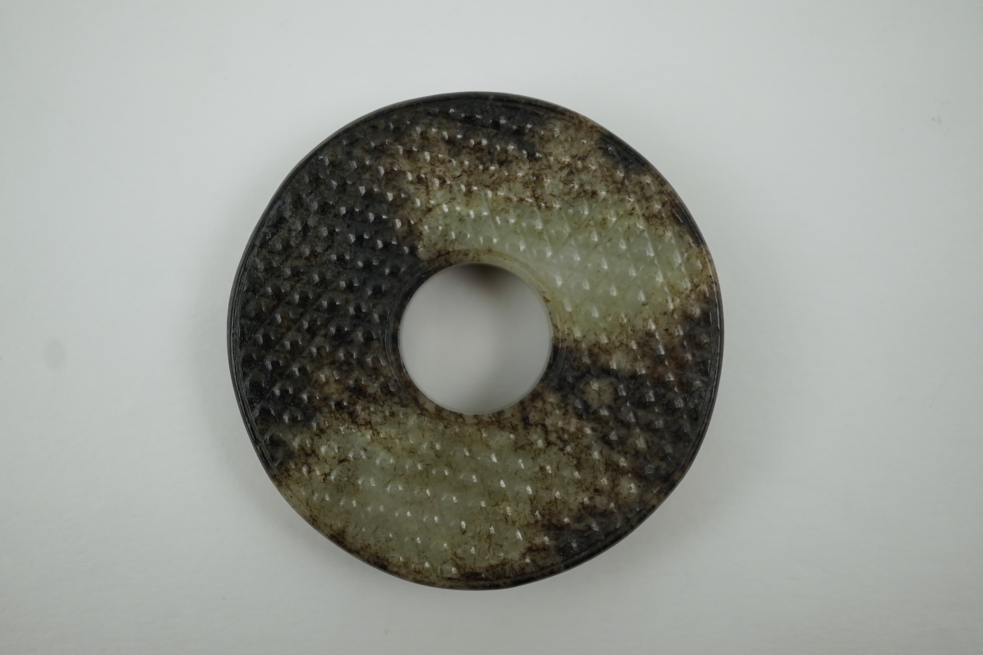 A Chinese pale celadon and black jade bi disc